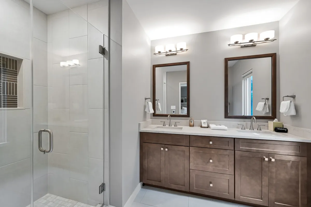 A spacious bathroom featuring a glass shower enclosure, double vanity with elegant mirrors, and soft lighting. The serene color palette and refined fixtures create a spa-like atmosphere ideal for self-care and relaxation.