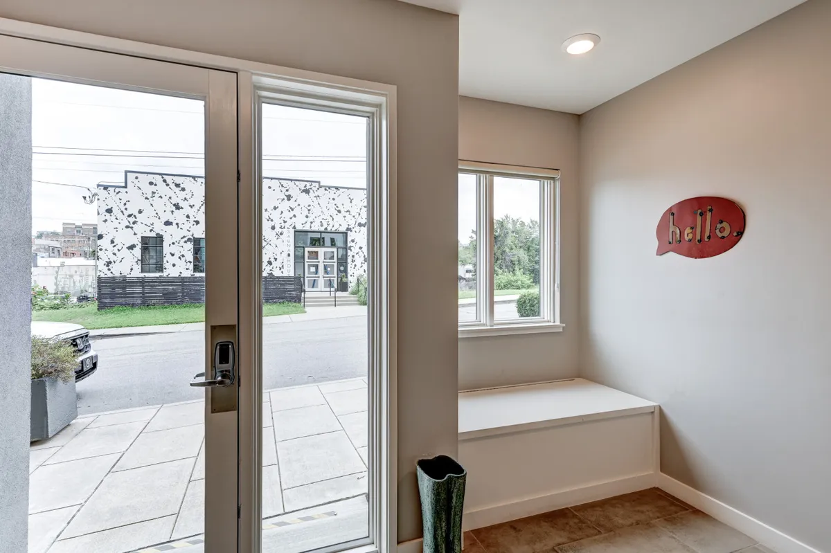A cozy view of the home's front door with a greeting sign and a window seat, suggesting both security and a comfortable spot to relax or people-watch. Natural light creates a warm, inviting mood ideal for welcoming guests or residents after city adventures.