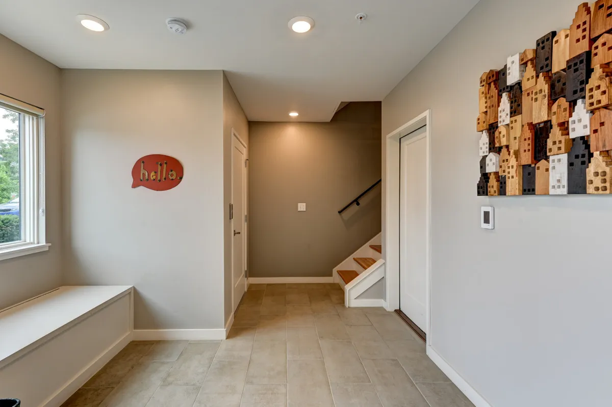 The image captures an inviting entryway with a 'hello' sign, a staircase, wooden wall art, and benched seating. The space feels warm and welcoming, perfect for greeting guests or group members as they return from exploring the area.