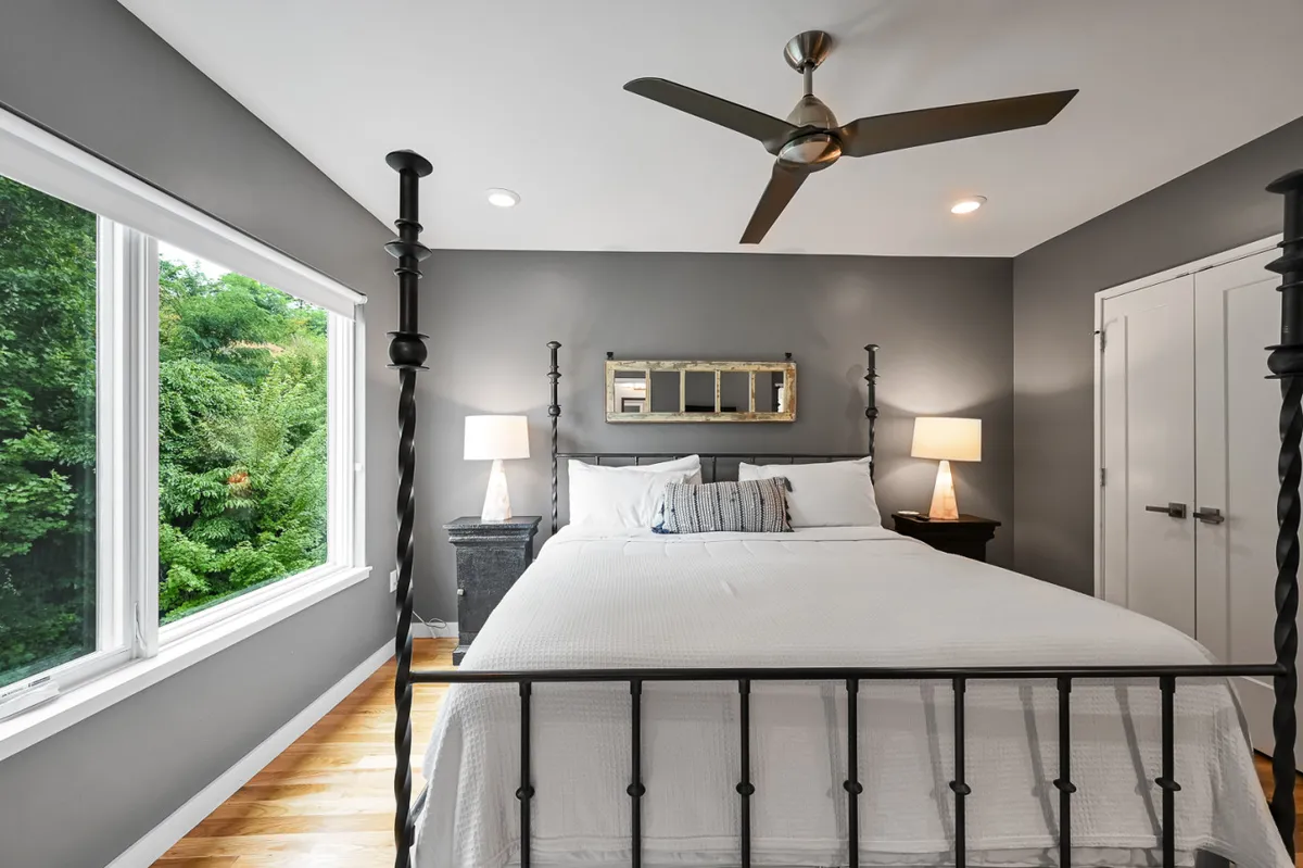 A tranquil king bedroom featuring a plush bed with crisp white linens, large window streaming in natural light, nightstands with soft-lit lamps, and modern wall art. The space is uncluttered, inviting, and designed for ultimate relaxation.