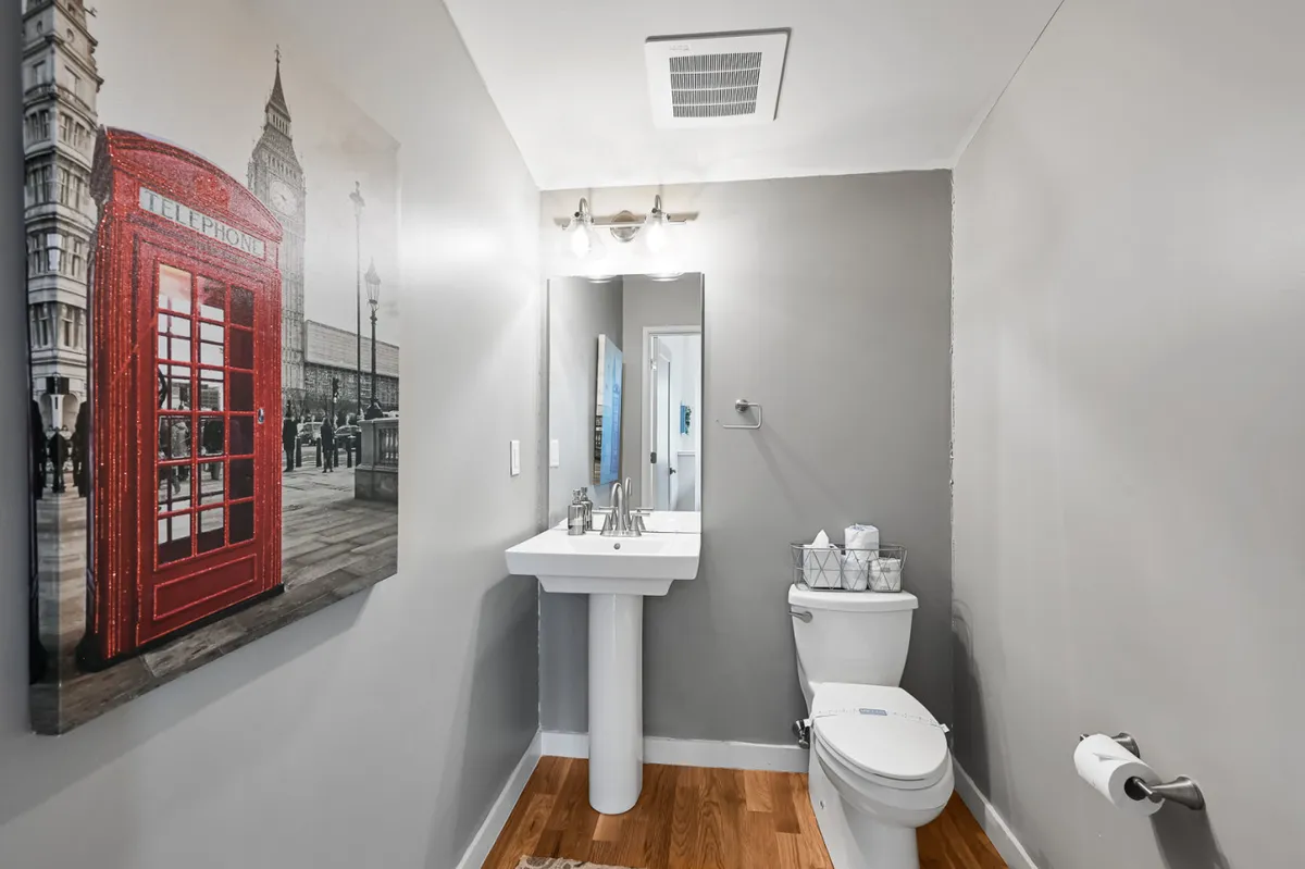 A modern, compact bathroom featuring a sleek sink, functional toilet, and a mirror with lighting. Unique decor, including a red telephone booth artwork, adds a playful touch. The space is designed for quick refreshment and personal grooming.