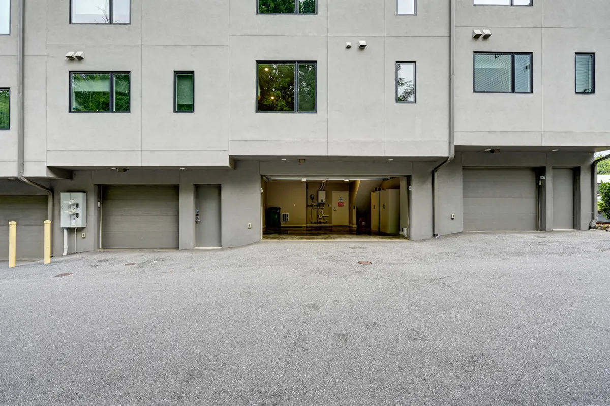 This image shows the exterior of the home, featuring two garage doors, several windows, and a simple concrete facade. The outdoor area suggests a practical and community-friendly environment, hinting at easy parking and group comings and goings.
