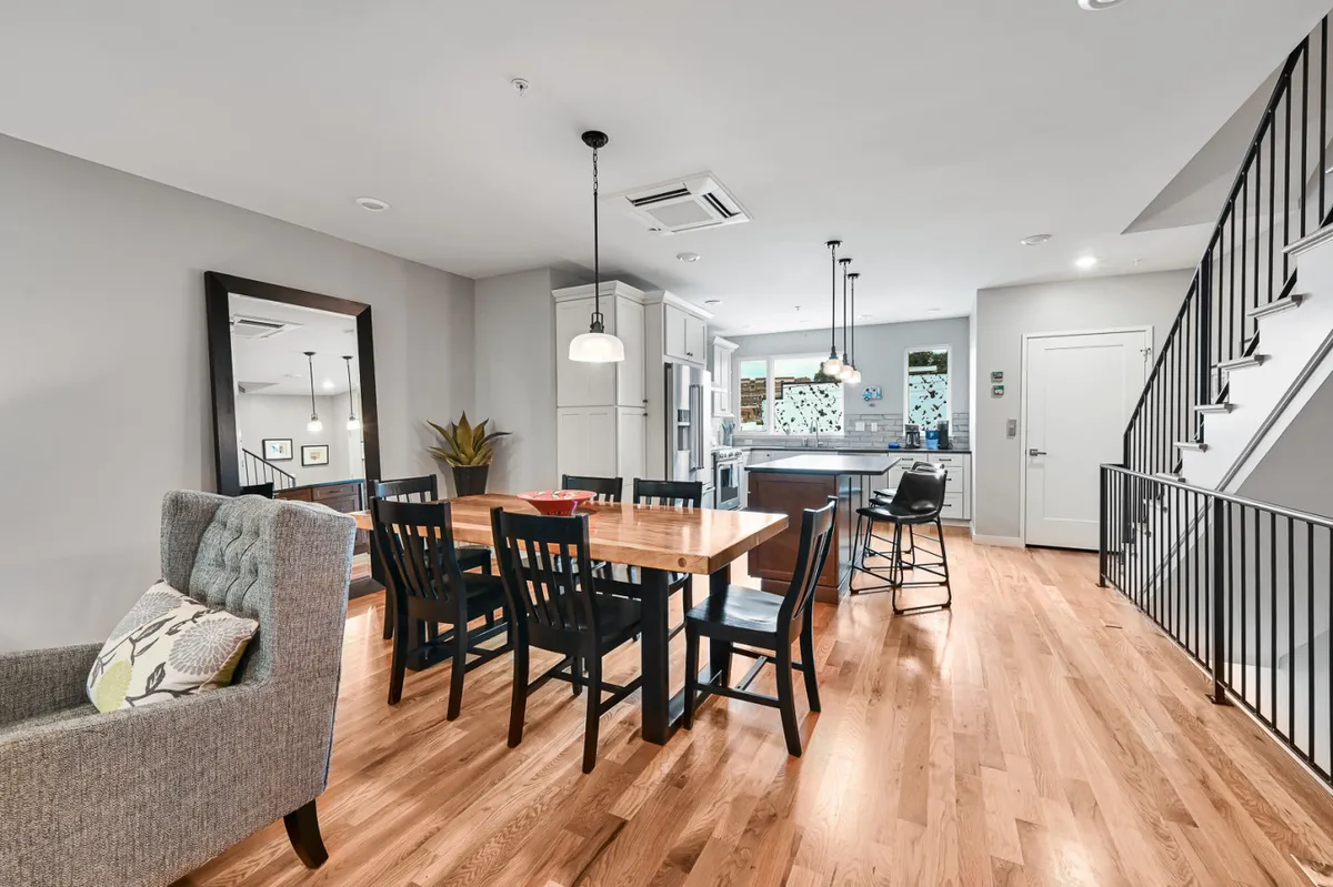An inviting dining area anchored by a large table with comfortable gray chairs, adjacent to a visible kitchen area. The mood is relaxed and sociable, ideal for shared meals or celebrations with friends and family.