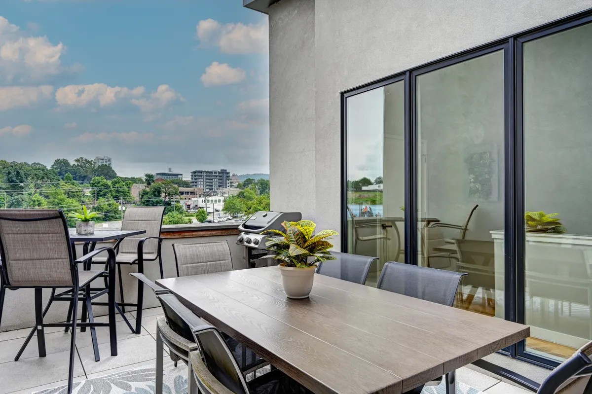 An inviting rooftop terrace set for outdoor dining, featuring a table, grill, planters, and an open view of the city skyline. The setting is perfect for gatherings, relaxation, and enjoying panoramic vistas at any time of day.