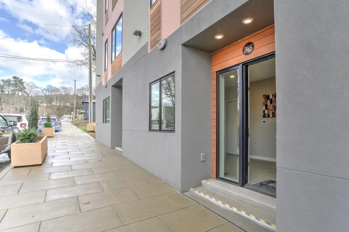 A modern building exterior featuring a welcoming entrance door, sleek architectural lines, and thoughtful landscaping elements that reflect an inviting, urban vibe. The scene suggests a lively, accessible location ideal for stepping out and exploring the surrounding neighborhood.