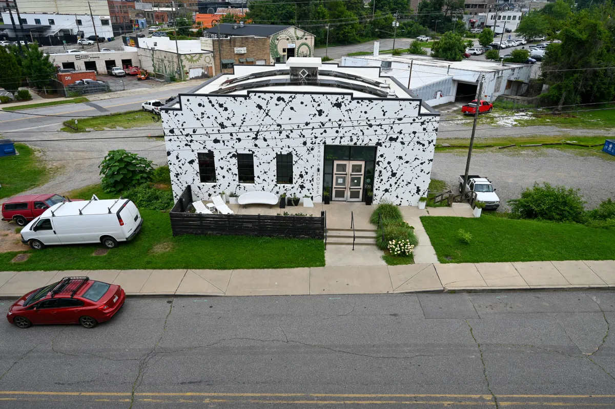 A striking black and white building facade with an outdoor seating area surrounded by greenery, alive with the feeling of community and artistic energy. The space is clearly designed for social gatherings, relaxation, and engaging with the creative local culture.