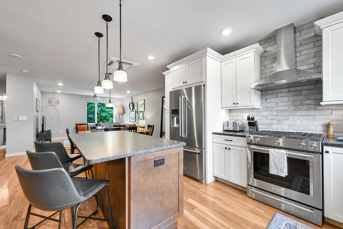 A modern open-plan kitchen with a large island, sleek stainless steel appliances, pendant lighting, and a seamless flow into the living/dining space. Sunlight pours in, highlighting the kitchen's welcoming design and making it perfect for both cooking and conversation.