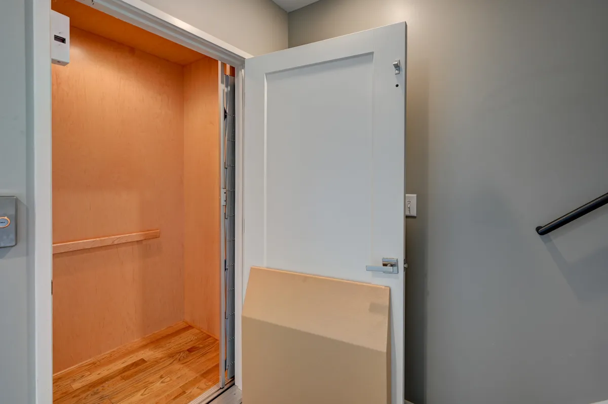 A modern, wood-floored elevator interior with an open door and neutral wall colors, emphasizing convenience and accessibility between floors within the property.