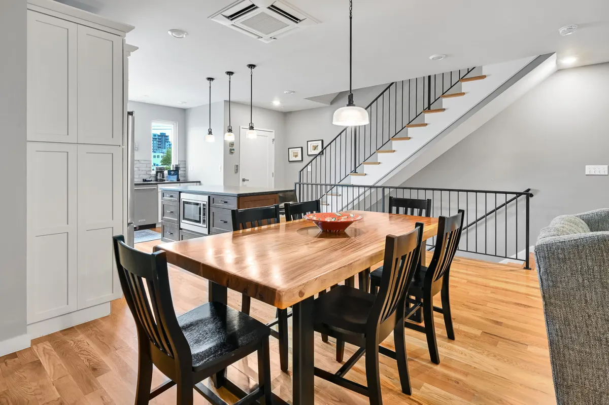 An open-plan dining area with a view of a staircase and a kitchen island, combining communal gathering spaces with a sense of vertical movement through the home. The stylish finishes and natural flow hint at luxurious, well-appointed living in a city-center setting.